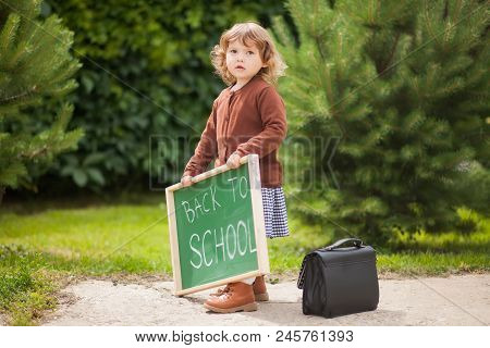 Cute Caucasian Little Girl Holding Chalkboard Written Back To School. With A Smile. Ready And Happy 