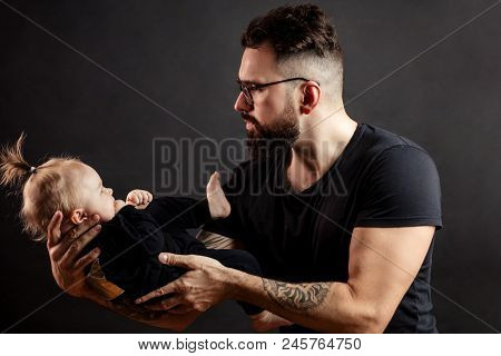 Happy Handsome Father In Perfect Fit, Looking At His Infant Baby Girl In His Hands, Fondling And Nur
