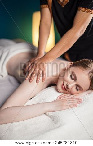 Beautiful Young Woman Lying With Closed Eyes On Table While Massage Therapist Massaging Her Shoulder