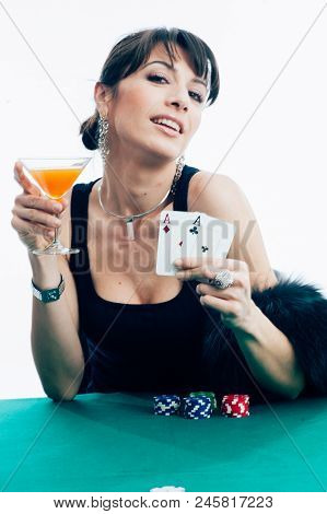 Young Caucasian Brunette Playing Poker At The Green Table Holding An Orange Aperitif Glass. Studio S