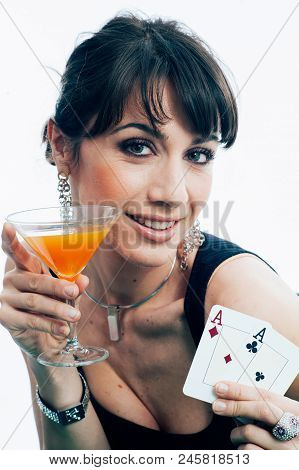 Young Caucasian Brunette Playing Poker At The Green Table Holding An Orange Aperitif Glass. Studio S