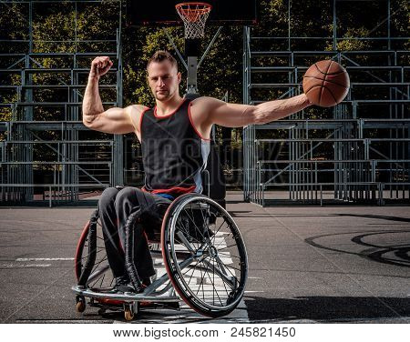 Strong Basketball Player In A Wheelchair Pose With A Ball On Open Gaming Ground.