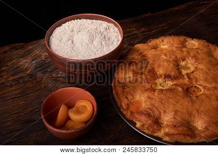 A Bowl With Flour And Apricot Cake On A Wooden Background On Black