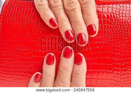 Close Up Red Lacquered Handbag In Woman Hands. Detail Of Red Leather Purse In Female Manicured Hands