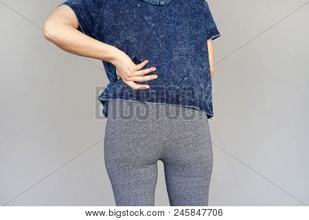 Close-up View Of A Young Woman With Pain In Kidneys Isolated On A Gray Background. Young Woman With 