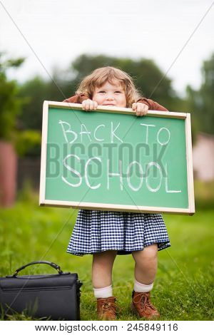 Cute Caucasian Little Girl Holding Chalkboard Written Back To School. With A Smile. Ready And Happy 