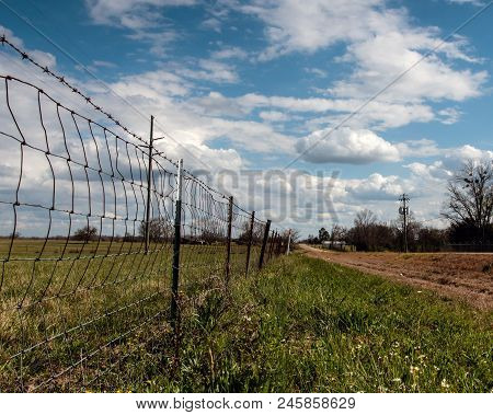 Wire Fence Leading Off Into The Distance With Perspective View With Blue Sky And Clouds