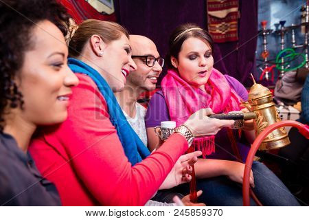 Group of friends smoking hookah and drinking coffee in shisha lounge enjoying themselves