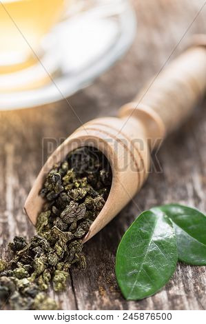 Spoon Of Dried Green Tea Leaves On Wooden Background. Leaves Of Green Tea Close Up