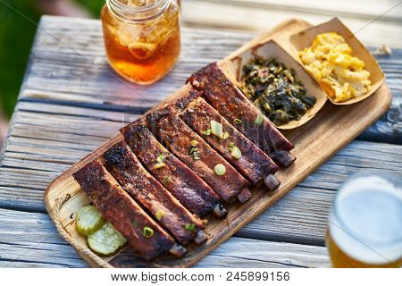st louis style bbq ribs with collard greens and mac & cheese outside on picnic table during sunny summer day