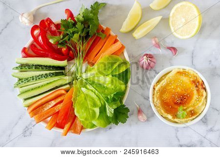 Hummus, Different Vegetables And Lettuce Leaves With Lemon And Garlic On A Light Background. Vegan F
