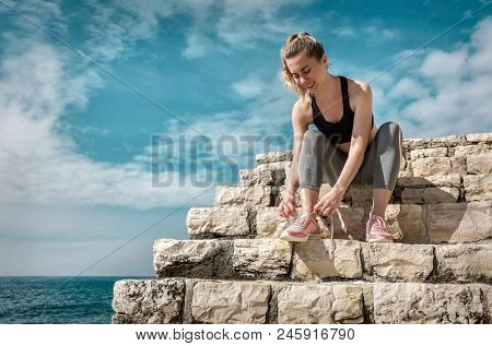 Women runner bootlace on her boot after running in sunny day under sunlight from blue sky near the sea.