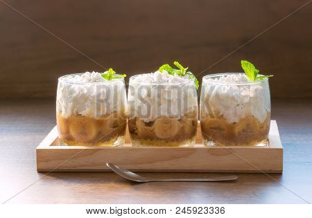 Three Banoffee Pie In A Cup.banoffee Decorated With Mint Leaves Placed In A Wooden Tray With Meal Se