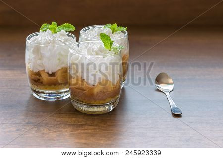 Three Banoffee Pie In A Cup.banoffee Decorated With Mint Leaves Placed In A Wooden Floor