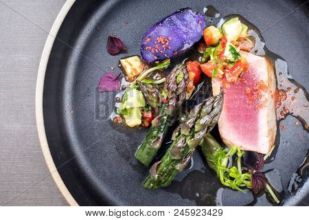 Modern fried tuna fish filet with green asparagus blue potatoes und vegetable chili relish as top view on a plate with copy space left 