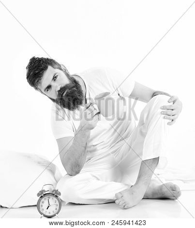 Sleepy Bearded Young Man Sit With Cup Of Coffee In Morning, White Background, Pillow And Alarm Clock