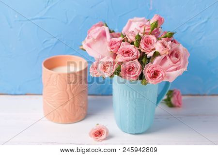 Background With Pnk Roses Flowers In Blue Cup  And Candle Against  Blue Textured Wall. Floral Still 