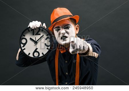 Scary Clown Pantomime With A Clock In His Hands, On A Dark Background.