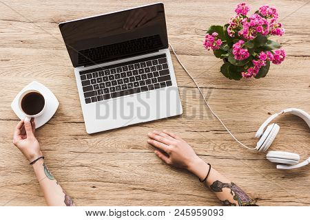 Partial View Of Woman At Tabletop With Laptop With Blanks Screen, Cup Of Coffee And Heaphones