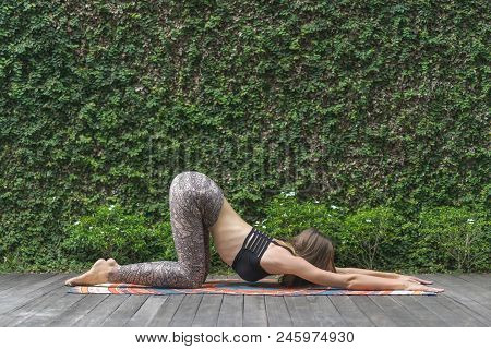 Side View Of Young Woman Practicing Yoga In Extended Puppy Uttana Shishosana Pose In Front Of Wall C