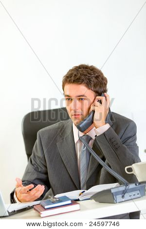 Vážné moderní podnikatel sedí v kanceláři a mluvící telefon