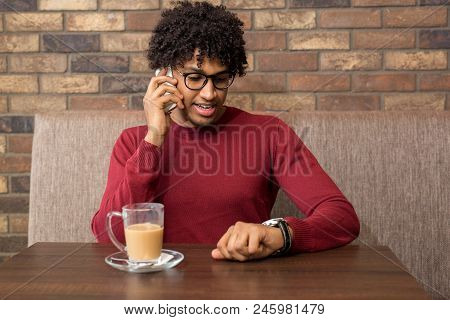 Handsome Young Businessman Talking On The Phone At A Cafe While Checking His Watch