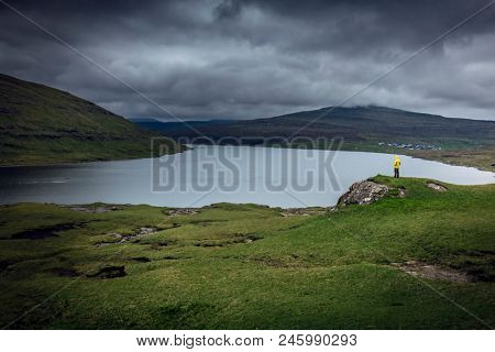 Man with yellow raincoat at SÃ¸rvÃ¡gsvatn lake in faroe island