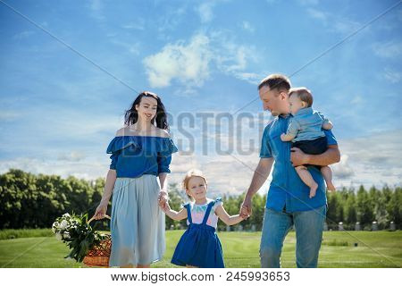 Happy Young Family Walking Down The Road Outside In Green Nature. Family With Children Go On Picnic