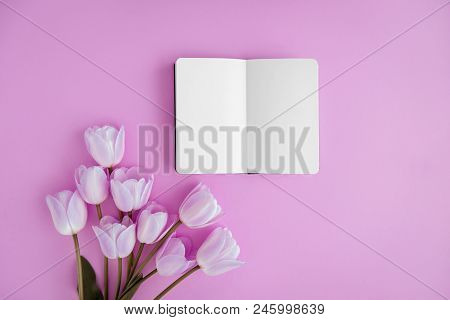 Opened Noteboog Around Beautiful Flowers. Violet Background. Flat Lay Style.