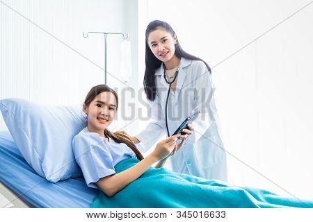 Asian Young Female Doctor Therapeutic Advising With Tablet To Asian Young Female Patient On Bed In H