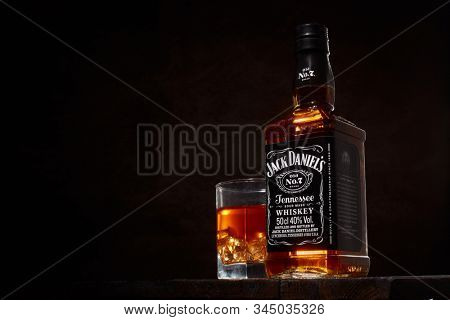St.Petersburg, Russia - December 2019 - Bottle of Jack Daniel's whiskey and glass with drink and ice  on wooden table on brown background with copy space. Brand of the American whiskey