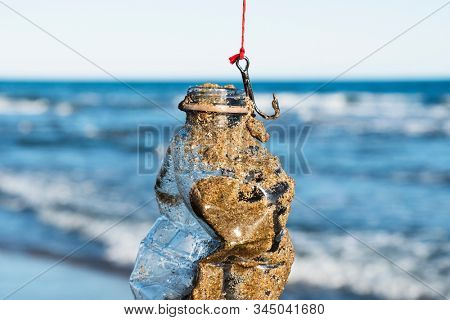 closeup of a used plastic bottle, covered with wet sand, in a fish hook, freshly fished in the ocean