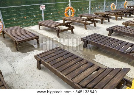Row Of Empty Wooden Beach Chairs Near Water.