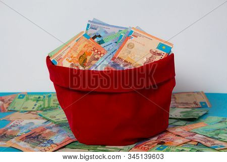Tenge In A Red Bag On The Background Of A Pile Of Money Kazakhstan, Kz, Kzt. Banknote, Paper Currenc