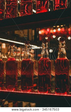 On The Shelf In The Bar Is Glass Bottles With Red Liquid