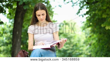 Beautiful female college student reading a book on a bench in a park