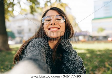 Happy Beautiful Young Woman Taking Self Portrait On Smart Phone During Relaxing Outside. Smiling Fem