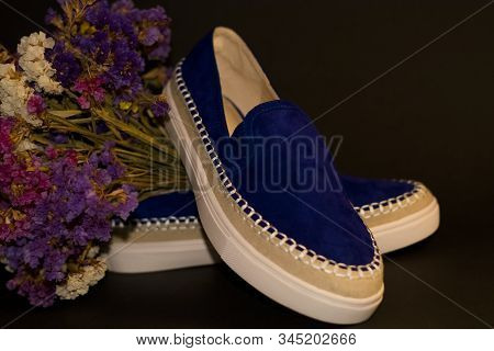 On Black Background, Pair Of Shoes, Blue Suede Slipons With White Thick Sole. Bouquet Of Dry Field F