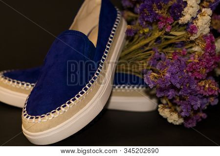 On Black Background, Pair Of Shoes, Blue Suede Slipons With White Thick Sole. Bouquet Of Dry Field F