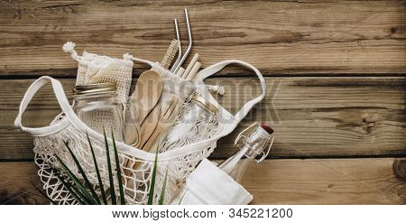 Mesh market bag with bamboo cutlery, reusable bottles and eco cotton bags on wooden background