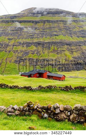 Breathtaking Faroe islands scenery with traditional red house with black roof
