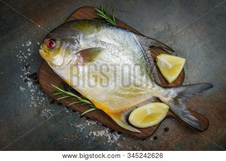 Fresh Pomfret Fish With Herbs Spices Rosemary And Lemon On Wooden Cutting Board And Black Plate Back
