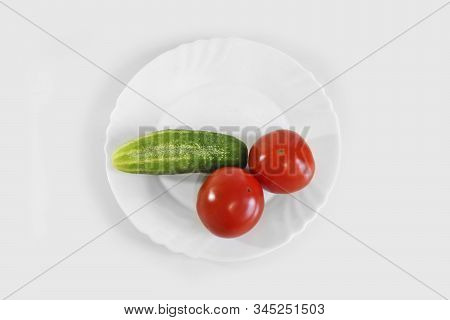 Red Ripe Juicy Tomatoes And Green Cucumber On A White Plate. The Phallic Image Of Natural Components