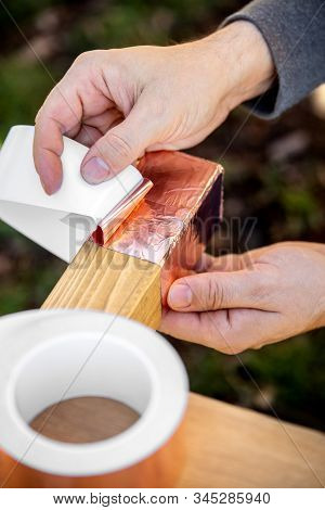 Man Is Affixing A Copper Tape On Wooden Beam, Barrier And Protection A Raised Bed For Home Gardening