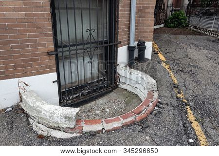 Ground Floor Window Covered In Iron Grate With Crumbling Window Well And Asphalt, Horizontal Aspect