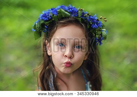 Portrait Of Beautiful 5 Years Old Girl With Blue Eyes In Wreath From Cornflowers Knapweeds In Summer