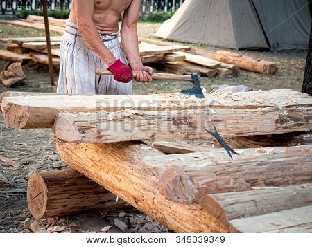 Carpenter Bare-chested In Medieval Cotton Clothes Working With Hardwood With An Ax. A Man Manually C