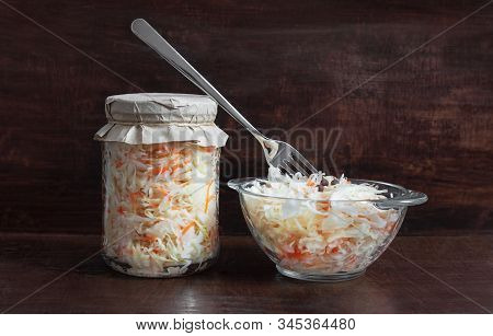 Homemade Sauerkraut With Carrots In A Glass Jar And Bowl On A Dark Wooden Background. Fermented Food