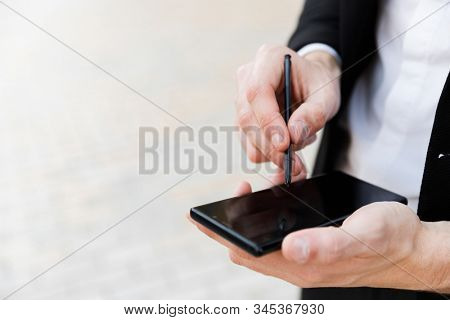 Close up of a businessman using mobile phone and stylus outdoors