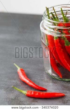 Close Up Of Thai Red Fresh Hot Chilli Peppers With Green Tails In In Clear Glass Jar Without A Lid, 